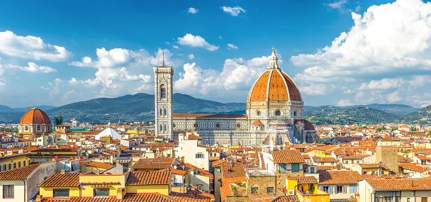 Top aerial panoramic view of Florence city with Duomo Cattedrale di Santa Maria del Fiore cathedral, buildings houses with orange red tiled roofs and hills range, blue sky white clouds, Tuscany, Italy