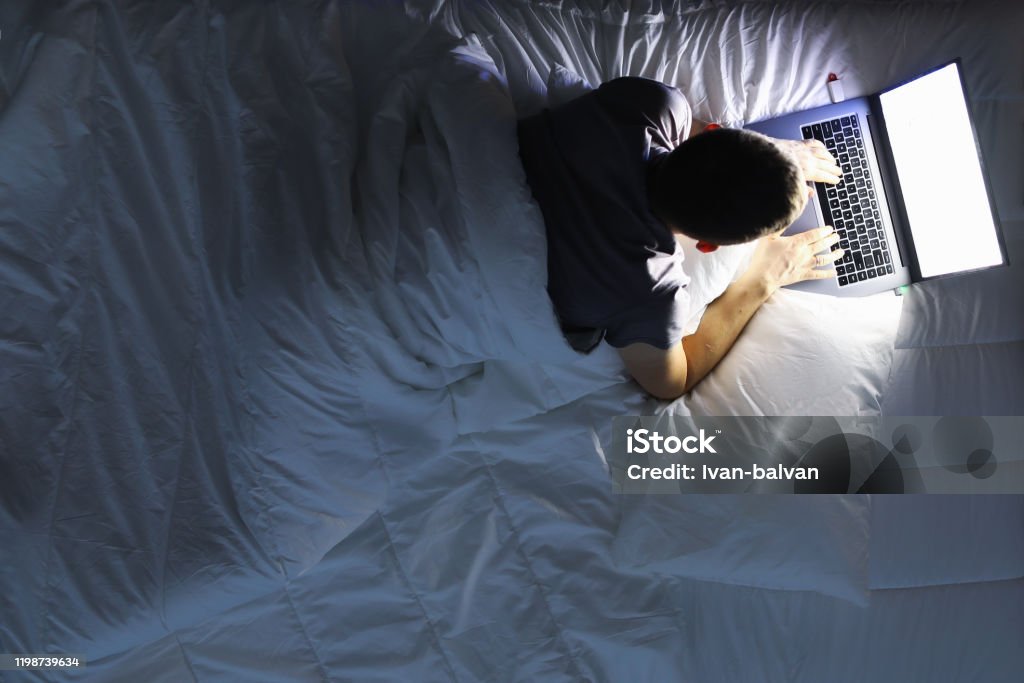 Man in bed with laptop using internet in online service Man in bed with laptop using internet in online service love chat closeup background. Round the clock helpline concept Bed - Furniture Stock Photo