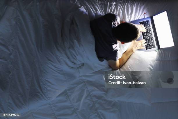 Man In Bed With Laptop Using Internet In Online Service Stock Photo - Download Image Now