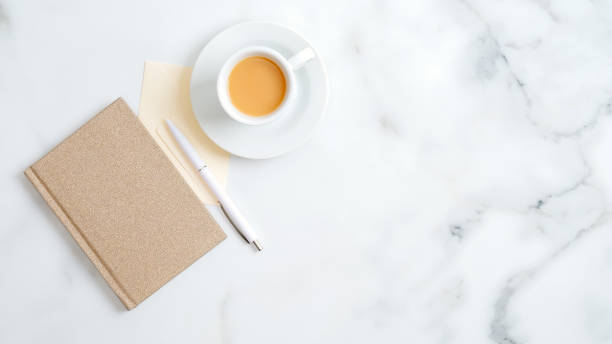 istock Minimal style home office desk top view. Flat lay feminine workspace with paper notebook, cup of coffee, pen on marble table. Woman work place, business concept. 1198740764