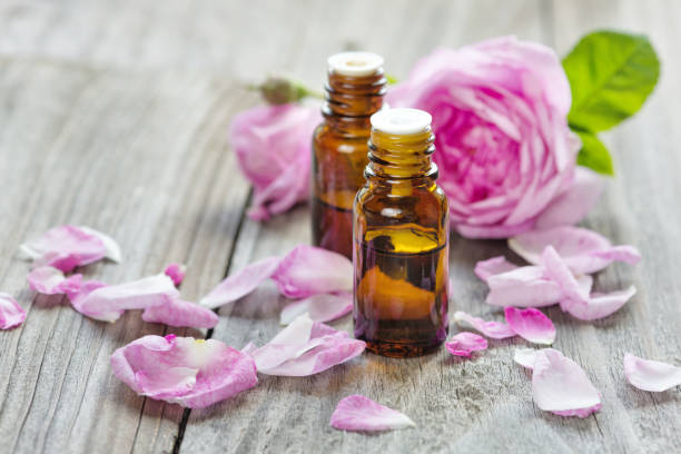Rose essential oil Two vials with essential oil and petals of pink roses on a wooden background alchemy photos stock pictures, royalty-free photos & images