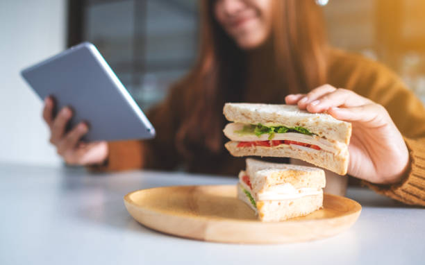 istock woman holding and eating whole wheat sandwich while using tablet pc 1198757695
