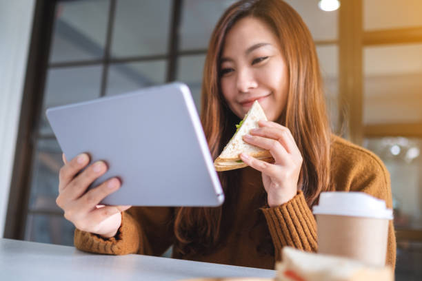 istock woman holding and eating whole wheat sandwich while using tablet pc 1198757710