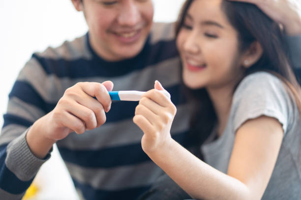 Close up shot of Asian couple feeling happy when see the pregnancy test result from testing kid. Man holding woman head and smile with happiness to be a father in future. Family relationship concept Close up shot of Asian couple feeling happy when see the pregnancy test result from testing kid. Man holding woman head and smile with happiness to be a father in future. Family relationship concept pregnancy test stock pictures, royalty-free photos & images