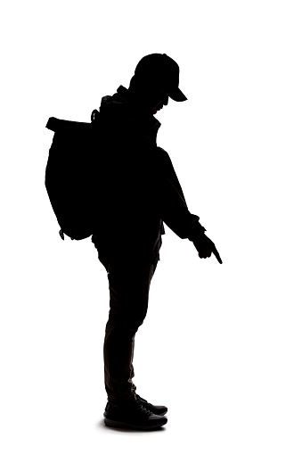 Silhouette of a man wearing a backpack looking like a traveler or hiker trekking.  He is pointing at something