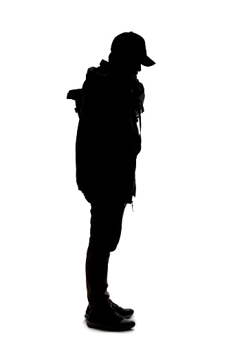 Silhouette of a man wearing a backpack looking like a traveler or hiker trekking.  He is patiently standing and waiting