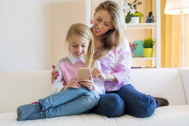istock Mom and daughter are using  phone while sitting on the couch 1198762218