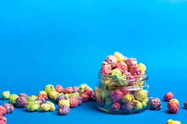 istock Multicolored fruit flavored popcorn in glass cups on blue background. Candy coated popcorn. 1198774387