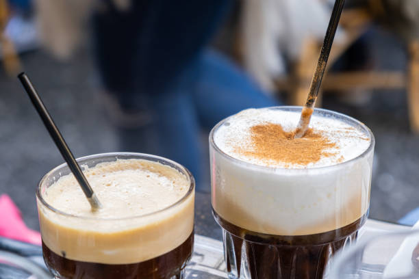 Two tall glasses of instant coffee with black straws. Freddo espresso and capuccino. A couple of tall glasses with cold instant coffee and black straws for a couple. Time to relax. Close up view, blur background. freddo cappuccino stock pictures, royalty-free photos & images