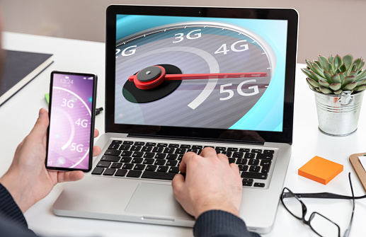 5G, internet speed test, high speed concept. Man holding a mobile phone, speedometer 5G speed network connection on the computer laptop screen, business office background.