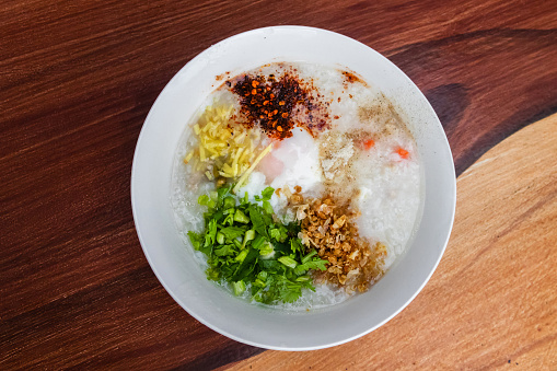 Rice congee with soft-boiled egg flavor with pickled chili vinegar and ground dried chilies on wooden table.