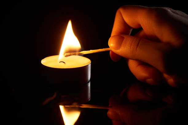 selective focus of woman lighting up candle with match isolated on black - fire match women flame imagens e fotografias de stock