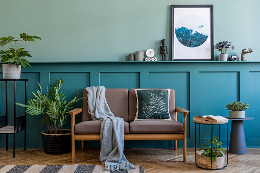 Elegante diseño interior de la sala de estar en el apartamento con sofá marrón, una gran cantidad de plantas, muebles de diseño y accesorios elegantes. Simular marcos de cartel en el estante. Paneles de madera verde. Puesta en escena en casa. photo