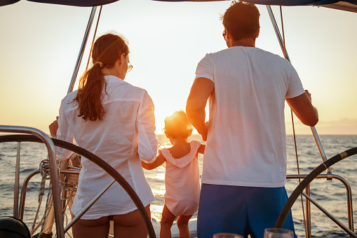 Beautiful happy family enjoying together their vacation on sailboat. They are sitting in cockpit and amazing sunset is in the background