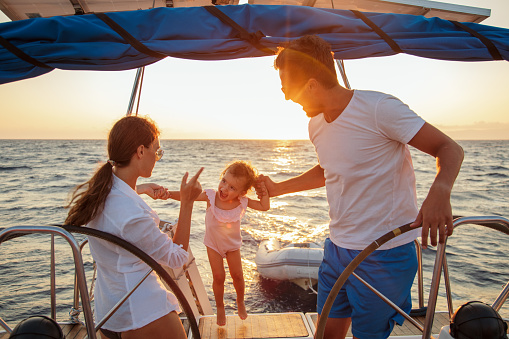 Beautiful happy family enjoying together their vacation on sailboat. They are sitting in cockpit and amazing sunset is in the background