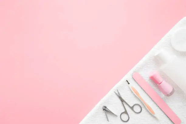 Manicure set on white towel. Empty place for text or logo on pastel pink table background. Flat lay. Top down view.