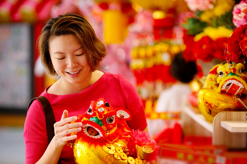 A female adult is holding decorative gold ingot with lion dance for Chinese New Year decorations cheerfully.