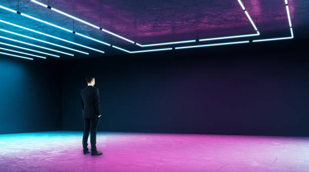 istock Businessman looking at copyspace dark wall in modern empty exhibition hall with neon paints. 1198810873