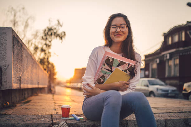 istock Shy girl holding her notebooks while sitting on stairs 1198814812