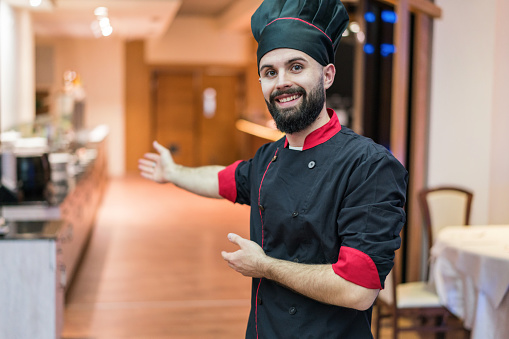 Charming young chef in the restaurant welcoming the guests