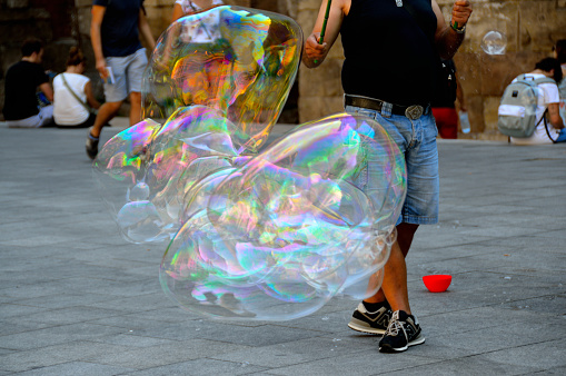 BARCELONA / SPAIN - August 2018: Man creates giant bubbles in the street and allows tourists to try for a fee. Parent photographs their child having a go.