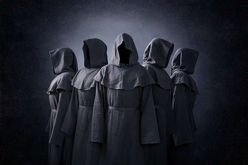 Group of five scary figures in hooded cloaks in the dark