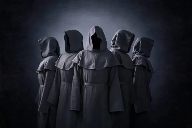 Group of five scary figures in hooded cloaks in the dark