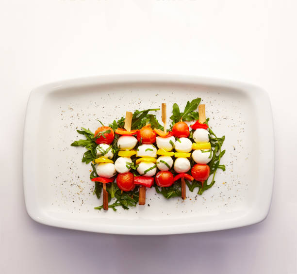 Directly above shot of Tomato, pepper and mozzarella skewers on a bed of dressed Rocket served in a plate