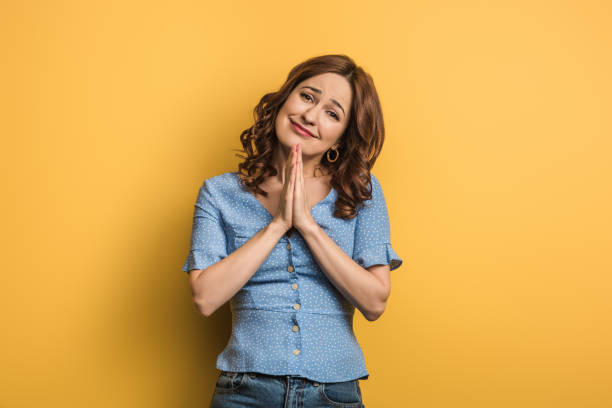 istock smiling girl showing praying hands while looking at camera on yellow background 1198835962