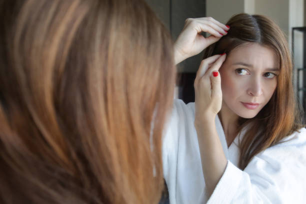 retrato de uma mulher nova bonita que examina seus scalp e cabelo na frente do espelho, raizes do cabelo, cor, cabelo cinzento, perda de cabelo ou problema seco do scalp - cabelo grisalho - fotografias e filmes do acervo