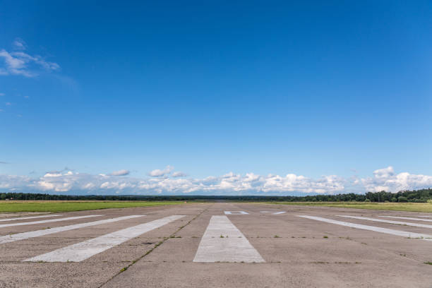 The runway of a rural small airfield against a blue sky The runway of a rural small airfield against a blue sky with clouds of the airfield. airplane hangar photos stock pictures, royalty-free photos & images