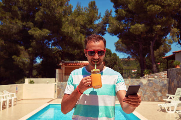 istock Attractive man using cellphone while drinking juice near swimming pool. 1198849375