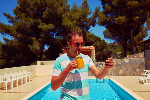 istock Attractive man using cellphone while drinking juice near swimming pool. 1198849428