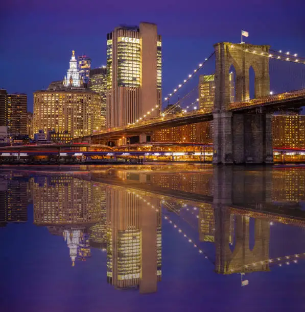 Photo of Brooklyn Bridge and Manhattan Municipal Building Reflected in East River at Sunset, New York, USA.