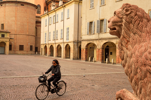 Reggio Emilia, Emilia-Romagna, Italy - April 21, 2019: A lady cycles through Piazza San Prospero which the locals call Lion Square because of its lion statues