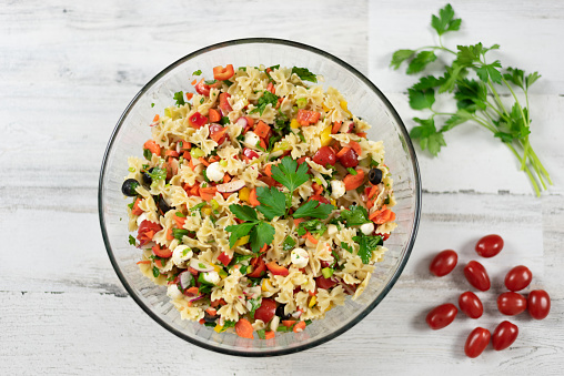 Top view of homemade pasta salad with fresh vegetables and herbs on a white wood background