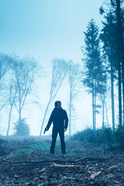 homme dans la veste noire avec le pistolet dans la forêt brumeuse d'hiver. - handgun gun blue black photos et images de collection