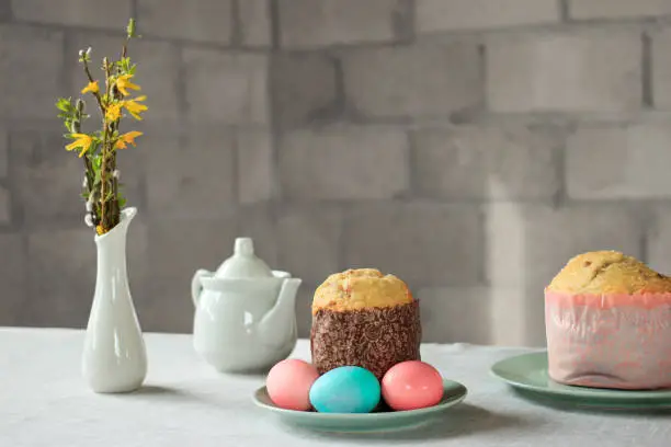 Photo of Pastel pink and blue Easter eggs, Russian and Orthodox Easter bread kulich or paska, vase with spring forsythia flowers and catkins of willow on table