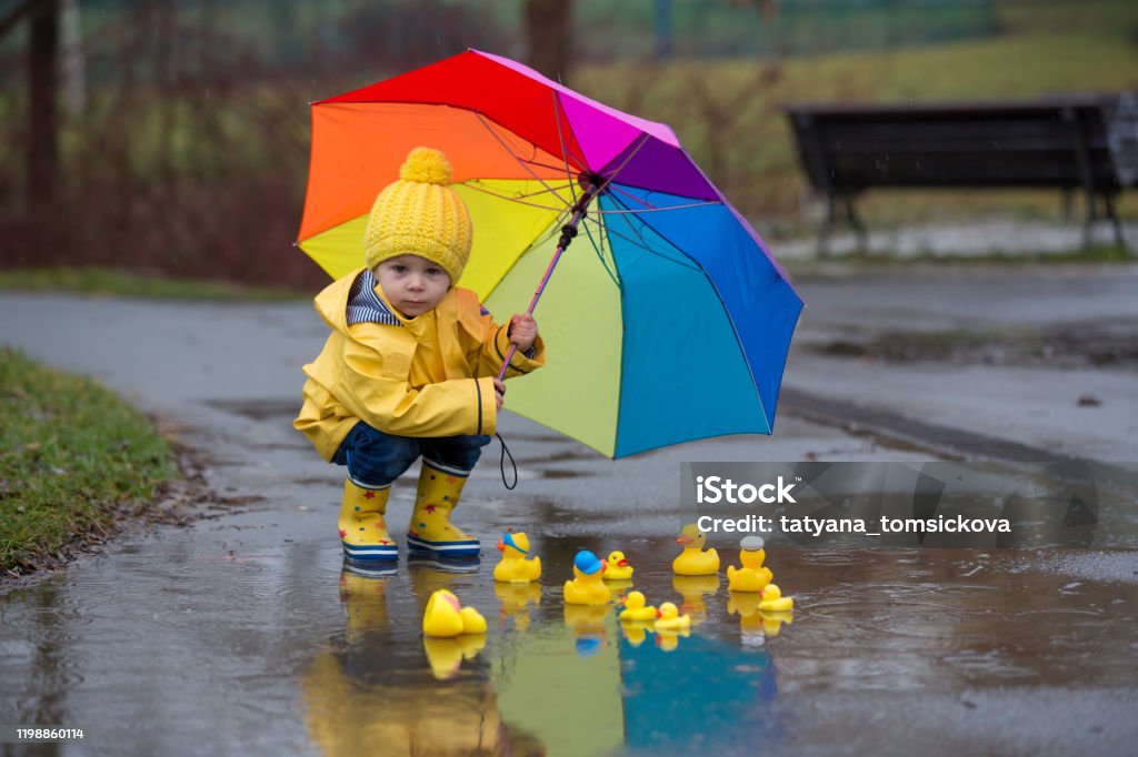 Schöne lustige blonde Kleinkind Junge mit Gummienten und bunten Regenschirm, springen in Pfützen und spielen im Regen - Lizenzfrei Kind Stock-Foto