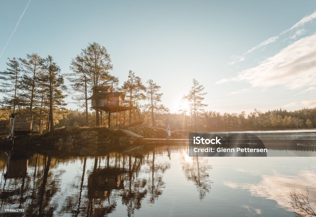 Woman walking by treetop cabin in Norway. December 7, 2019 - Fiddan, Norway -  Treetop cabin by calm lake. Autumn Stock Photo