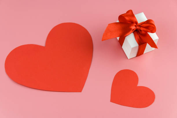 istock white gift box with red strap and two paper crafted hearts on a colour background, engagement ring box 1198863692