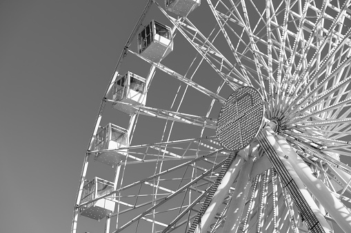 Big ferris wheel is spinning on gray background. People are riding panoramic weel and enjoy city view. Low angle view, copy space and macrophotography