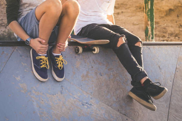 primer plano de dos jóvenes sentados en la media rampa de la tubería, después de buenos trucos y saltos en el skatepark. adolescentes de moda disfrutando del tiempo libre en el parque de patinaje. concepto de juventud, unión y amistad. - monopatín actividades recreativas fotografías e imágenes de stock