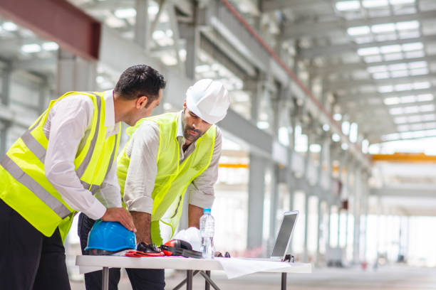 Middle Eastern Male Construction Professionals Onsite Close-up of Abu Dhabi male design professionals in 20s and 30s examining blueprints and discussing development plans at construction site. architect onsite stock pictures, royalty-free photos & images