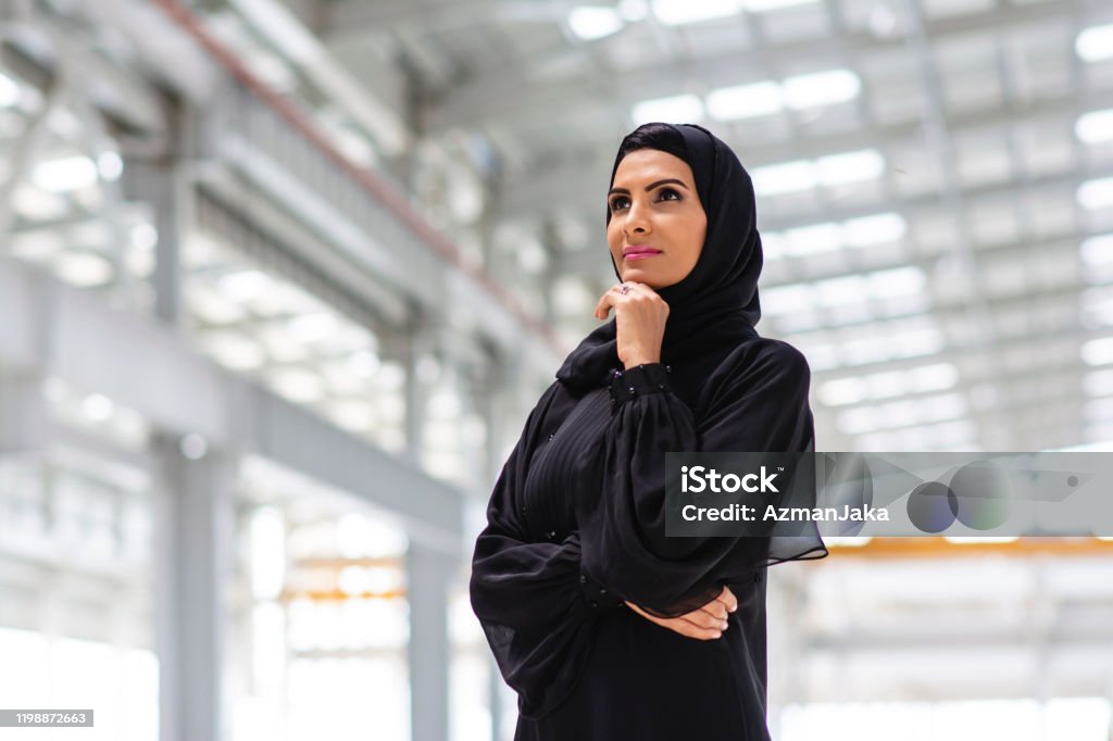 Portrait of Contemplative Middle Eastern Design Professional Low angle close-up of female construction professional in traditional Islamic clothing with hand on chin and observing development of Abu Dhabi site. United Arab Emirates Stock Photo