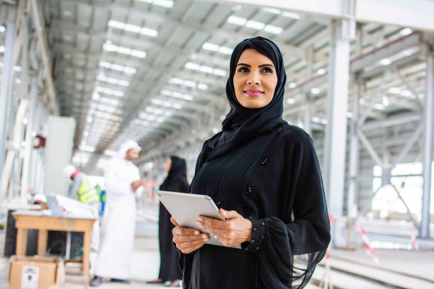 Abu Dhabi Construction Professional Using Digital Tablet Close-up of female design professional in traditional Islamic clothing using digital tablet and looking away from camera at Abu Dhabi construction site. emirati culture photos stock pictures, royalty-free photos & images