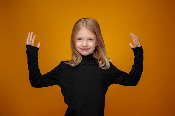 cheerful little girl with long blond hair and both arms raised stock photo