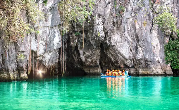 Photo of Cave entrance of Puerto Princesa subterranean underground river with longtail boat - Wanderlust travel concept at Palawan exclusive Philippine destination - Vivid filter with bulb torch light sunflare