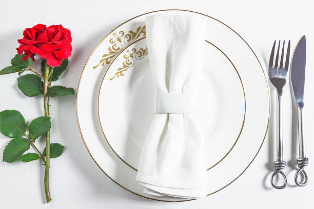 istock Romanitc table setting for Valentine's day dinner. White napkin with ring on white plates, beautiful cutlery and one red rose flower on a white background. 1198902770