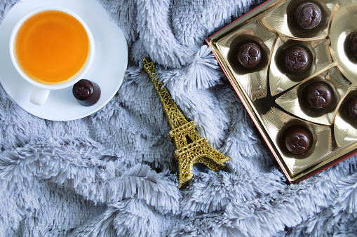 A cup of green tea, a box of chocolates and an eiffel tower figurine on a fur blanket.